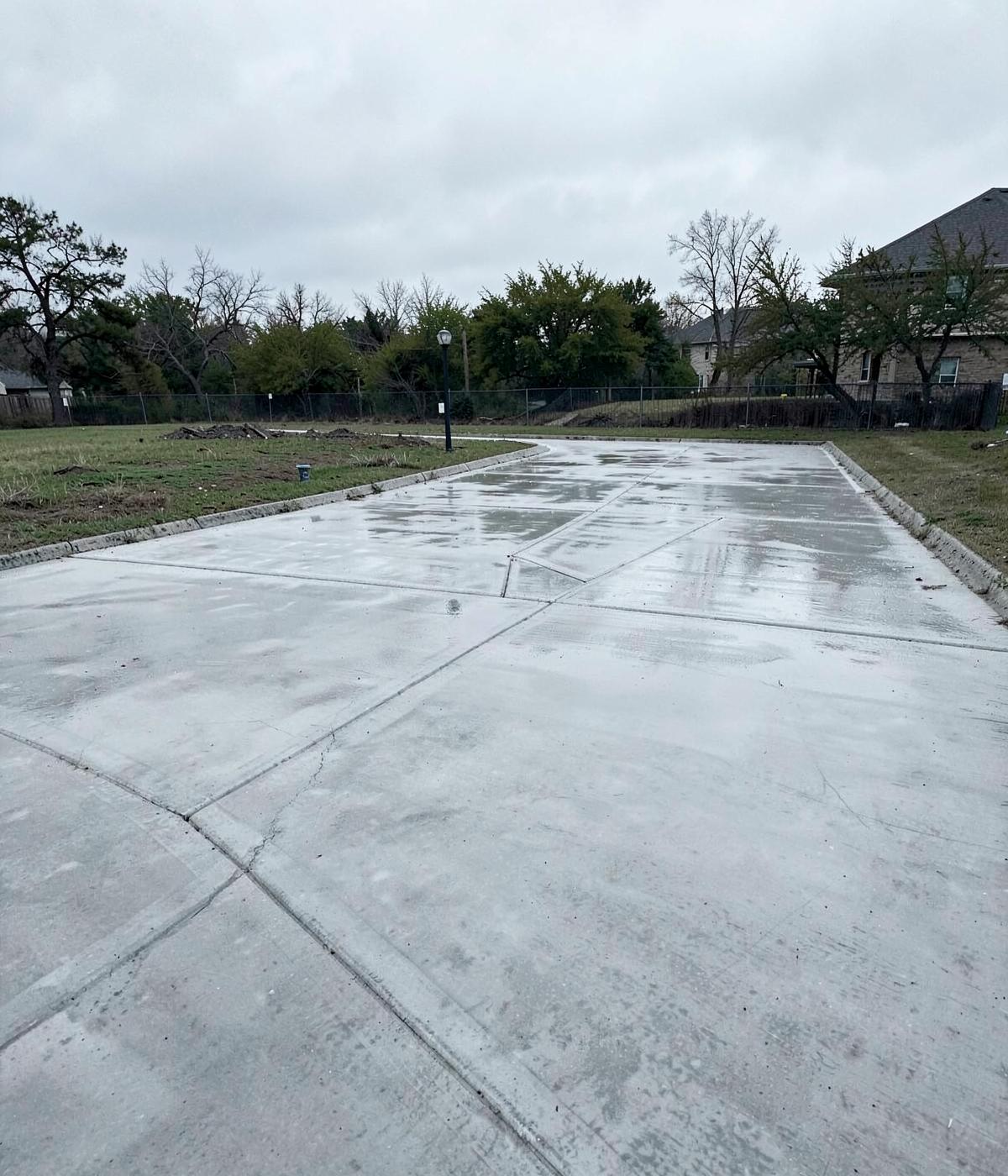 Freshly poured concrete driveway slab with saw-cut control joints under overcast Texas sky